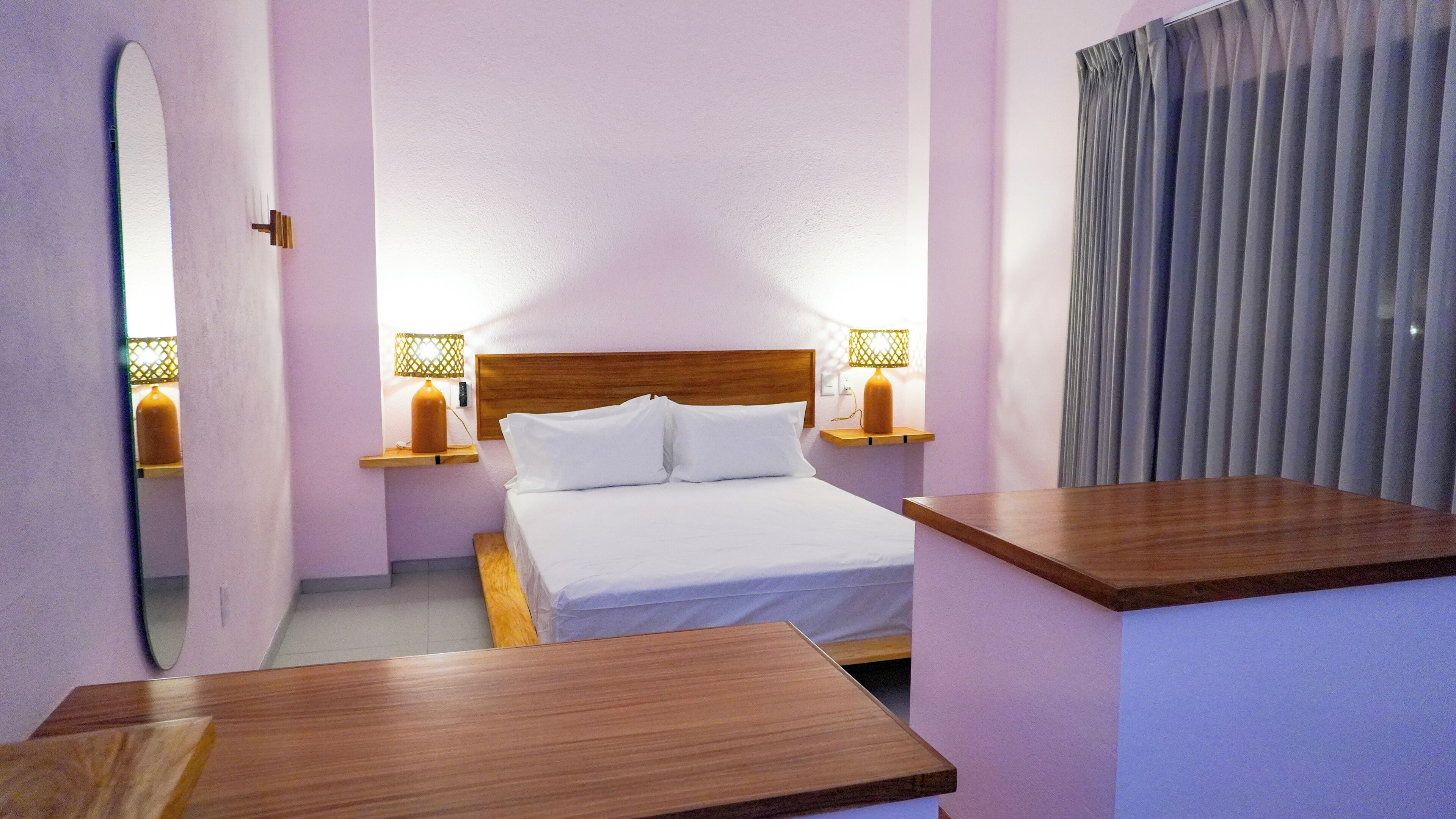 A hotel room with a wooden bed, two bedside tables with lamps, a mirror, and a window with curtains.