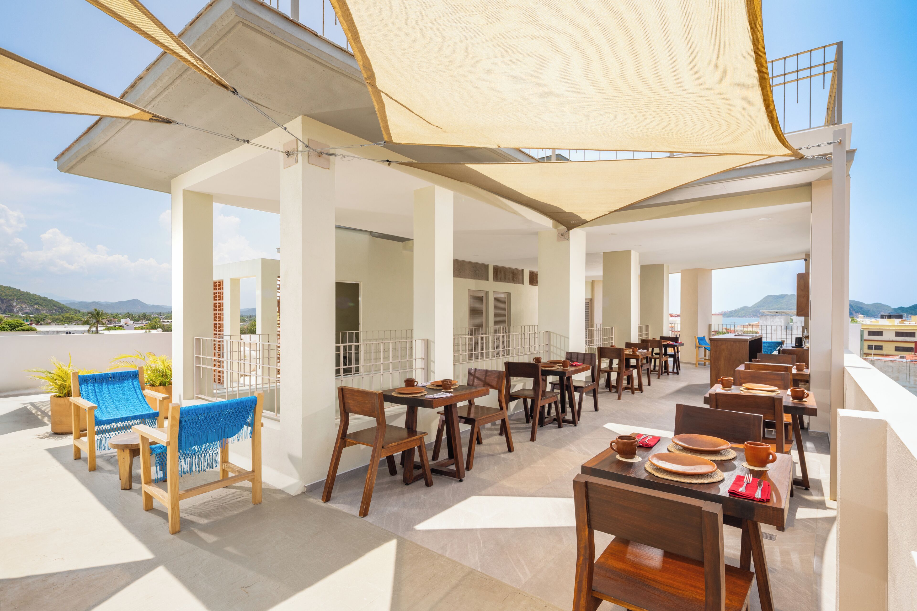 Una terraza en la azotea con mobiliario exterior, incluyendo mesas y sillas de madera, y vistas del paisaje circundante.