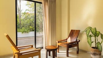 A room with two wooden chairs, a small round table, a potted plant, and a sliding glass door leading to an outdoor area with greenery.