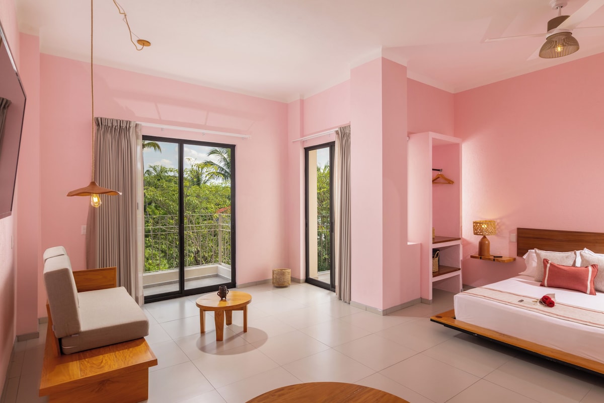 Una camera d'albergo con un letto, un'area salotto, un tavolino e un balcone con vista sul verde.