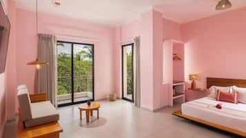 Habitación de hotel con cama, zona de estar, una mesita y balcón con vistas a zonas verdes.