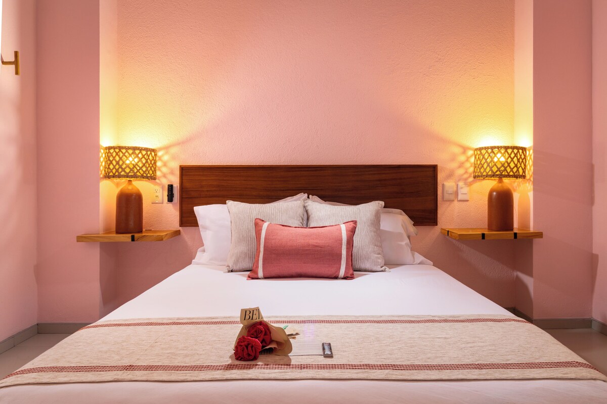 Habitación de hotel con una cama grande, dos lámparas de noche, un cabecero de madera y una mesita de noche con lámpara.