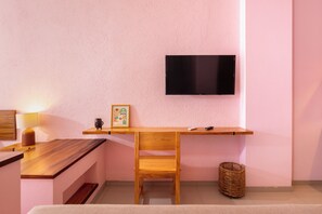 Una habitación moderna con un escritorio de madera, una silla, un televisor montado en la pared y una pequeña estantería con un marco de fotos y una taza.