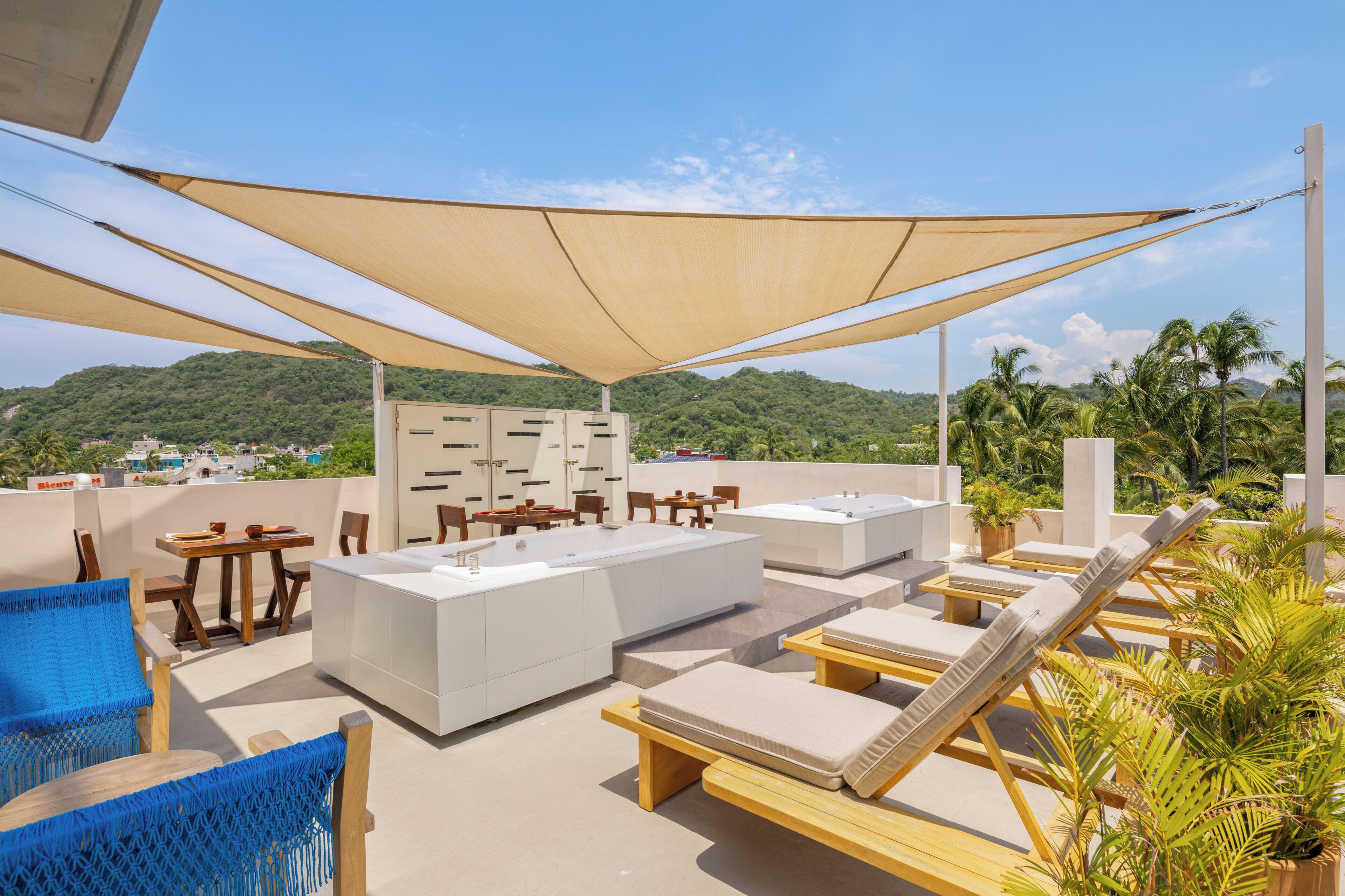Una terraza en la azotea con sillones de descanso, una zona de bar y vistas a un paisaje verde.