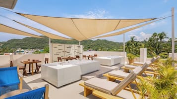 Una terraza en la azotea con sillones de descanso, una zona de bar y vistas a un paisaje verde.