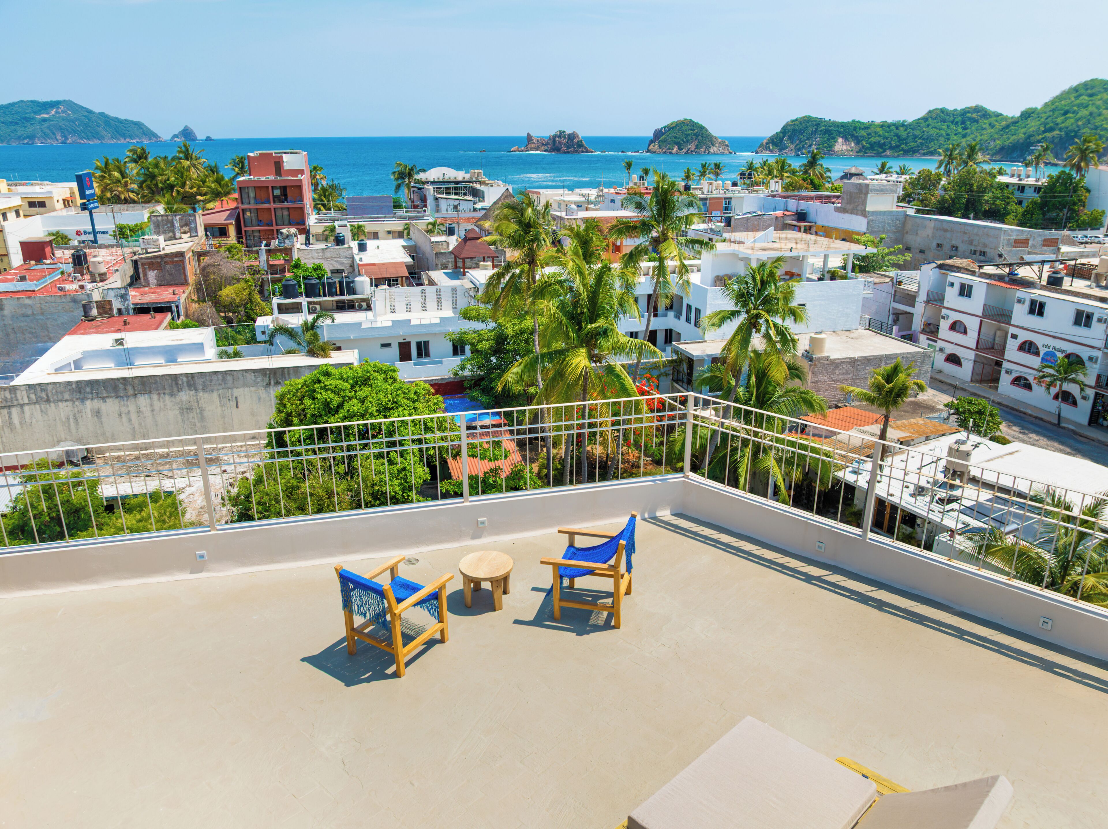 Una terraza en la azotea con vistas al mar, palmeras y edificios.