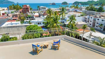 Una terraza en la azotea con vistas al mar, palmeras y edificios.