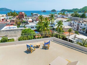 A rooftop terrace with a view of the sea, palm trees, and buildings. - Hotel Tepalcates (San Patricio Melaque)