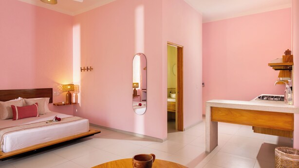 Een hotelkamer met een bed, nachtkastje, lamp, spiegel en uitzicht op de badkamer.