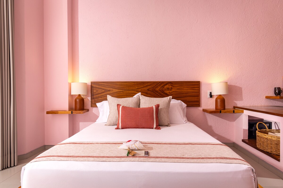 Een hotelkamer met een groot bed, twee nachtkastjes met lampen, een houten hoofdeinde en een wandplank met een mandje.