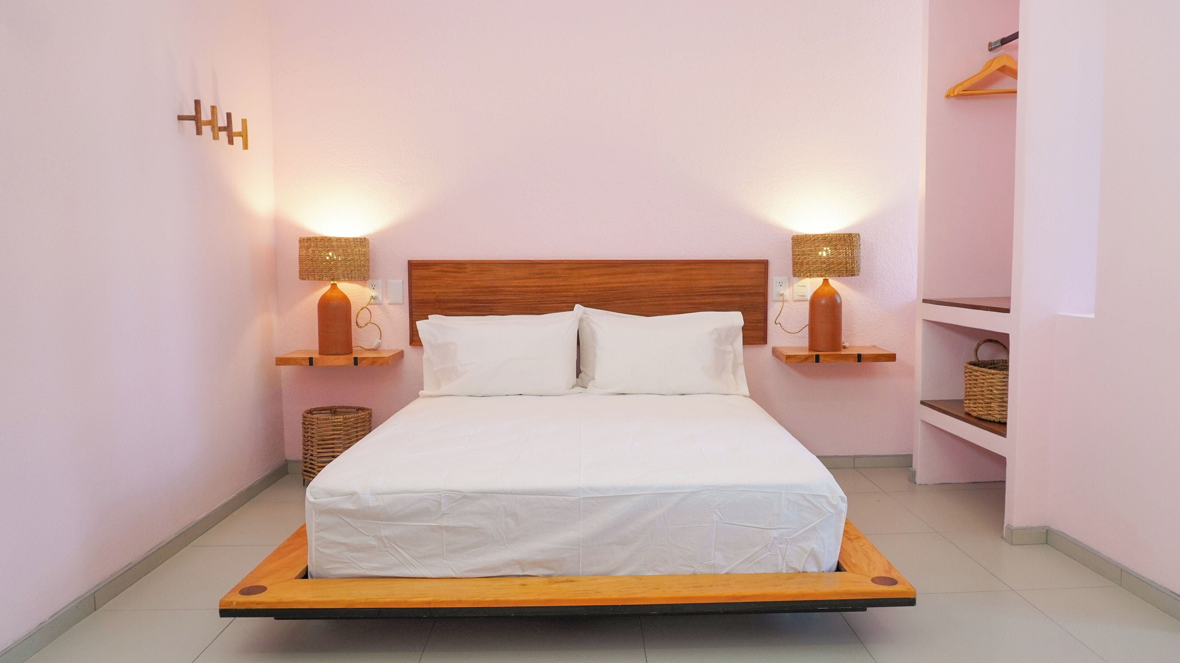 A bed with a wooden frame, two bedside tables with lamps, and a wall-mounted shelf with baskets.