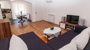 A modern living room with a sofa set, a dining table with chairs, a TV, and a kitchen area in the background. - Sunny Elegant Crikvenica Apartments (Crikvenica)
