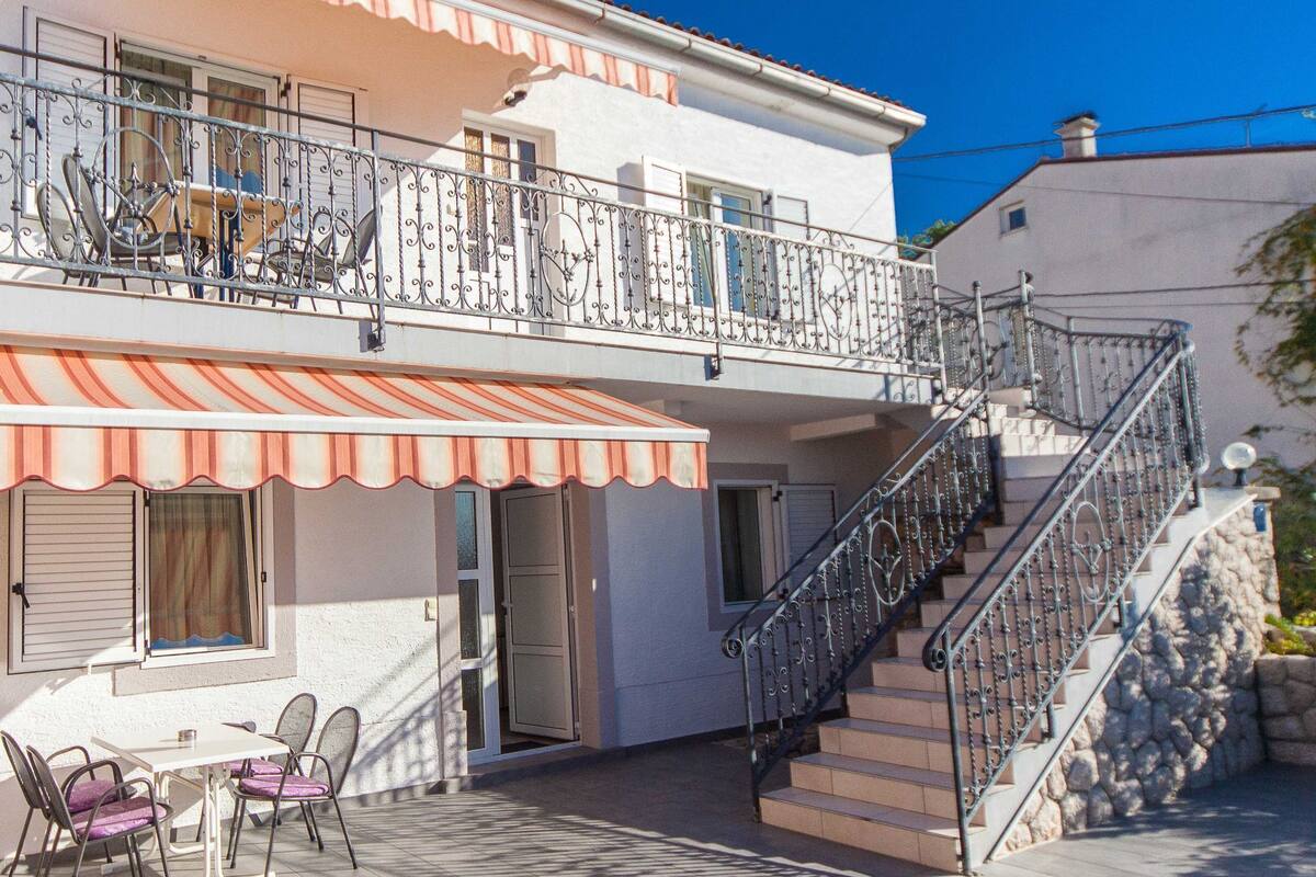 Ein zweigeschossiges Gebäude mit Balkon, Außenbestuhlung und einer Treppe.