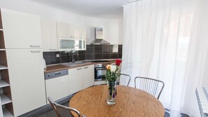 A modern kitchen with white cabinets, a stainless steel oven, and a wooden dining table with chairs. - Sunny Elegant Crikvenica Apartments (Crikvenica)