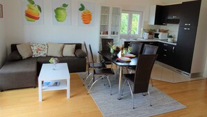 A modern living room with a sofa, a dining table with chairs, and a kitchen area with cabinets and a microwave. - Seaside Escape Selce Apartments (Crikvenica)