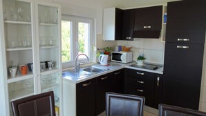 A compact kitchen with a sink, a microwave, and dark cabinets. There is a window providing natural light and a view of greenery outside. - Seaside Escape Selce Apartments (Crikvenica)