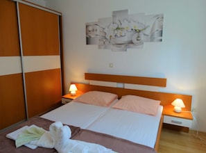 A bedroom with a bed, two bedside tables with lamps, a wall-mounted artwork, and a wooden wardrobe.