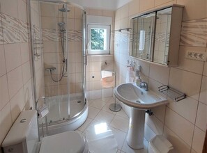 A modern bathroom with a glass-enclosed shower, a pedestal sink, and a large mirror.