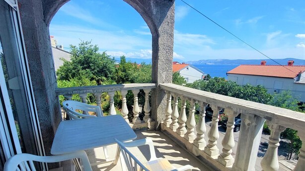 Een balkon met een tafel en stoelen, een stenen balustrade en uitzicht op zee en bergen.