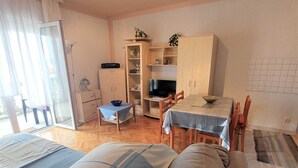 Een ruimtelijke zithoek met een bank, eettafel, stoelen, een televisie en een kitchenette.