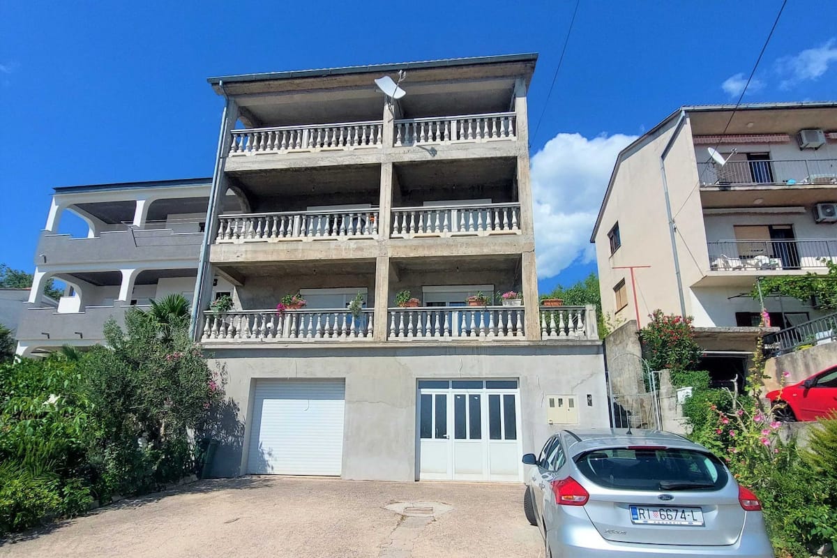 A multi-story residential building with balconies, a garage, and a parked car.