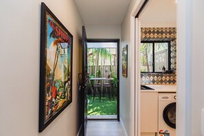 A narrow hallway leading to a patio with a table and chairs, a washing machine, and a framed picture on the wall.