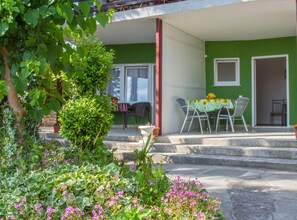A green building with a covered outdoor seating area, steps leading up to a door, and a garden with pink flowers. - Contemporary Crikvenica Apartments With Private Parking (Crikvenica)