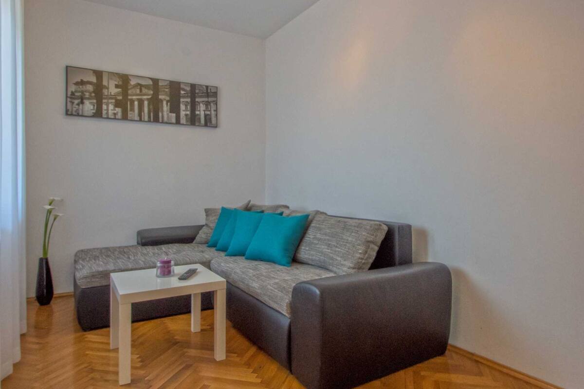 A living room with a grey sofa, a small white table, and a vase with flowers.