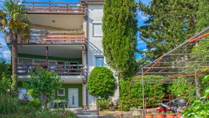 Un bâtiment à deux étages doté d’un balcon, d’un jardin avec des plantes en pot et d’une structure métallique.