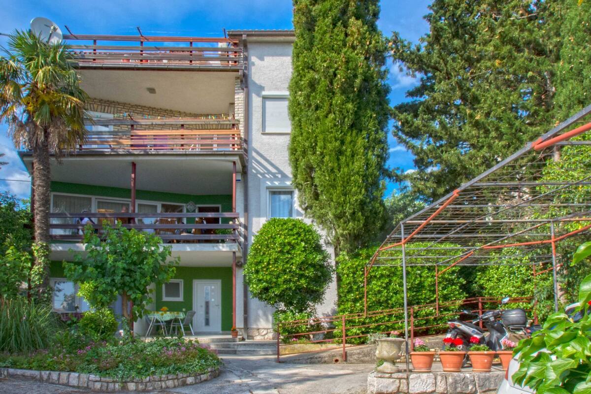 A two-story building with a balcony, a garden with potted plants, and a metal structure.