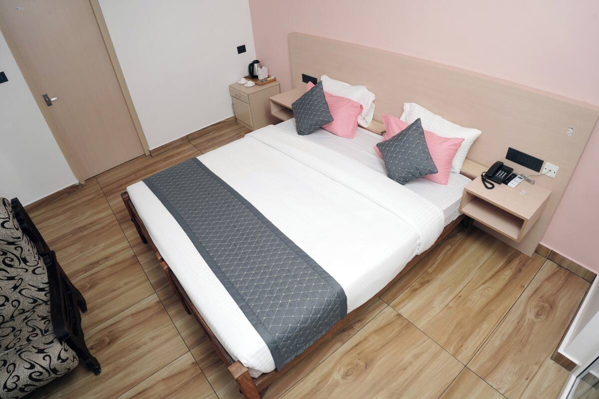 Ein ordentlich bezogenes Bett mit einer gesteppten Decke, ein Nachttisch mit Telefon und ein Beistelltischchen mit Lampe.