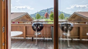 Eine Holzdielen-Terrasse mit zwei Grillanlagen, einem Holzzaun und Blick auf eine gebirgige Landschaft.