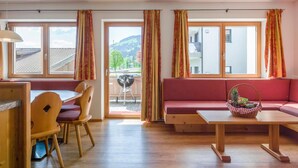 Ein modernes Wohnzimmer mit Esstisch aus Holz, einem roten Sofa und einem Balkon mit Grill.