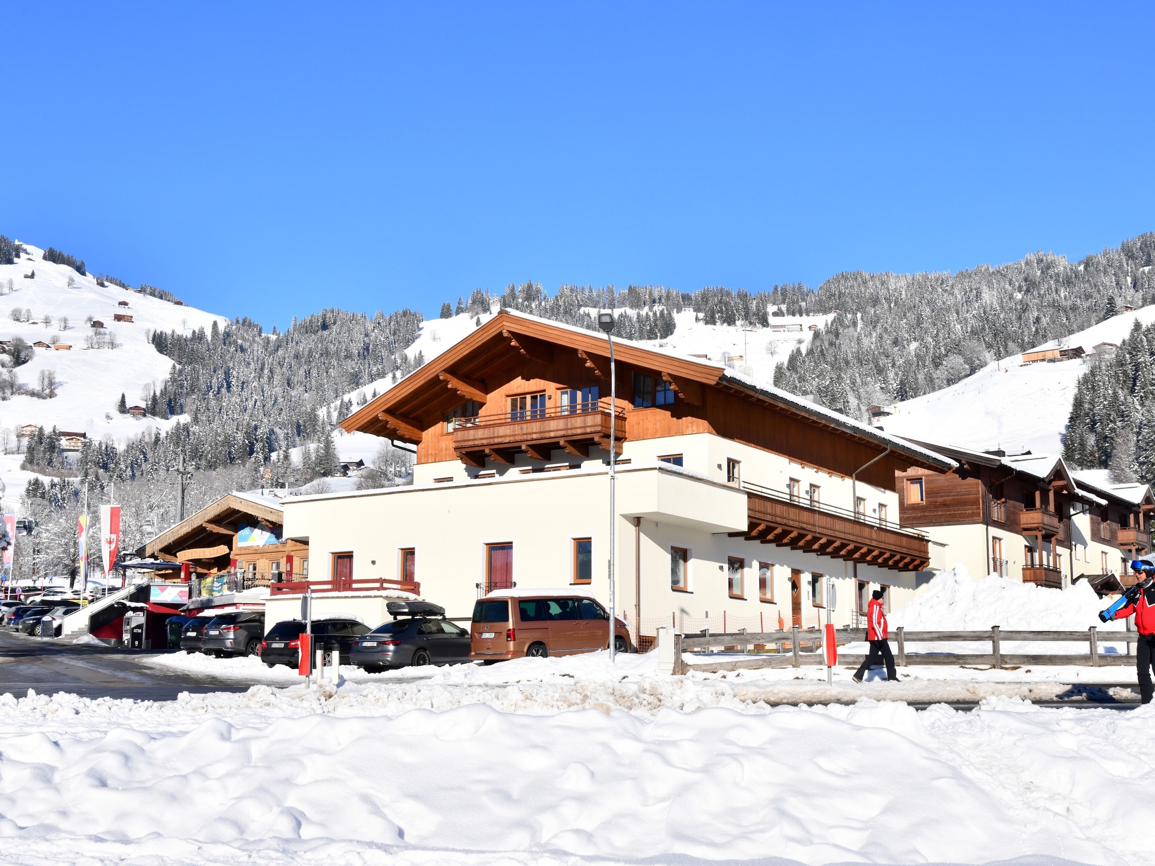 Un hôtel à la façade en bois, doté de nombreux balcons, avec une piste de ski en arrière-plan.
