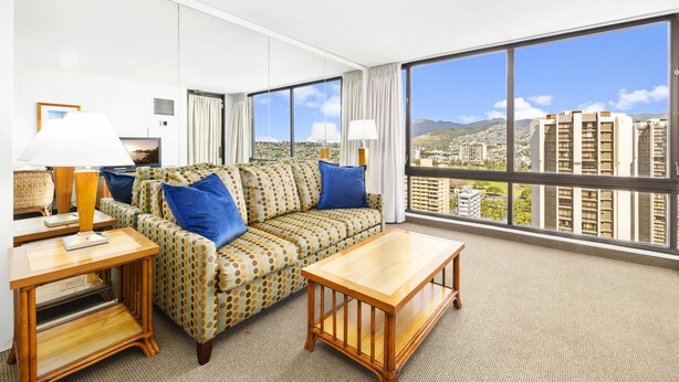 A hotel room with a large window, a sofa, a coffee table, and a lamp.