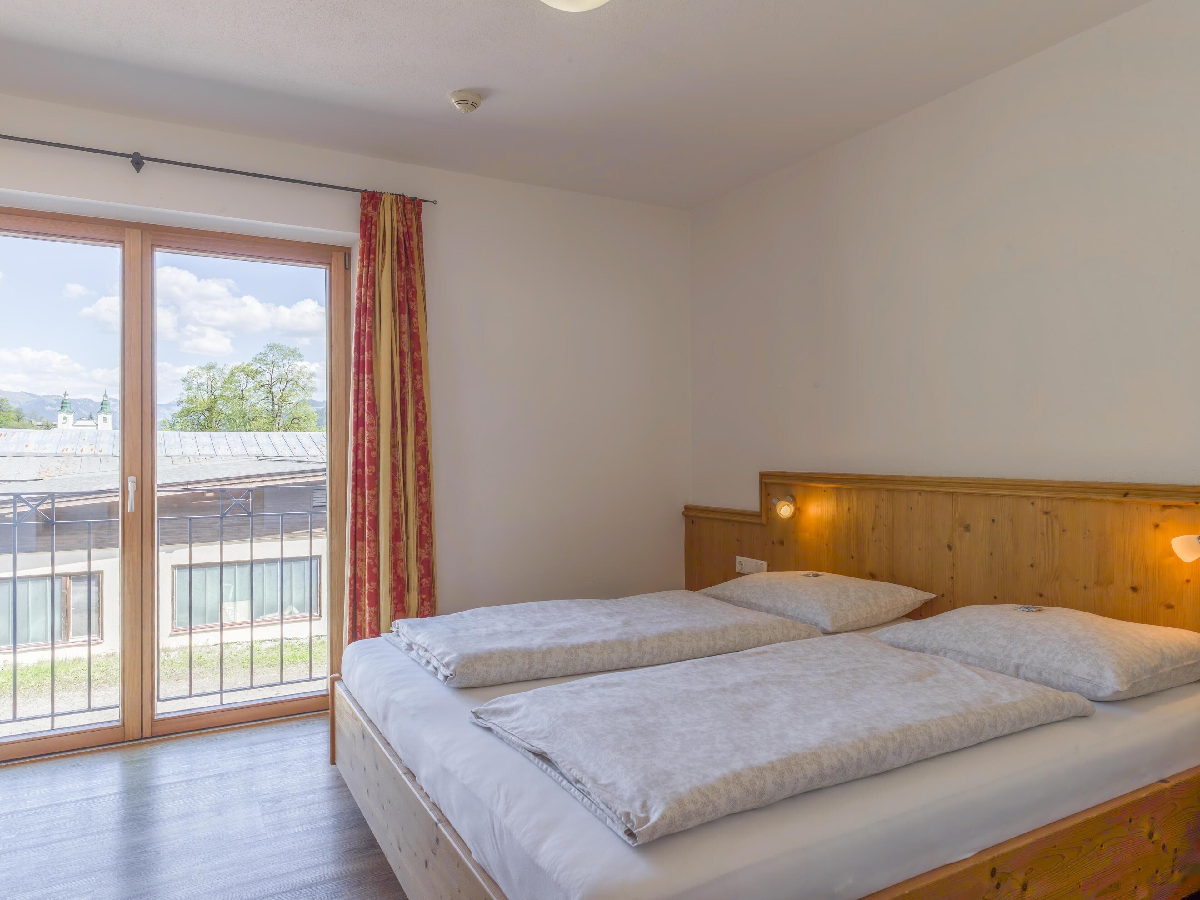 A double bed with a wooden headboard and a large window with a view of buildings and trees.