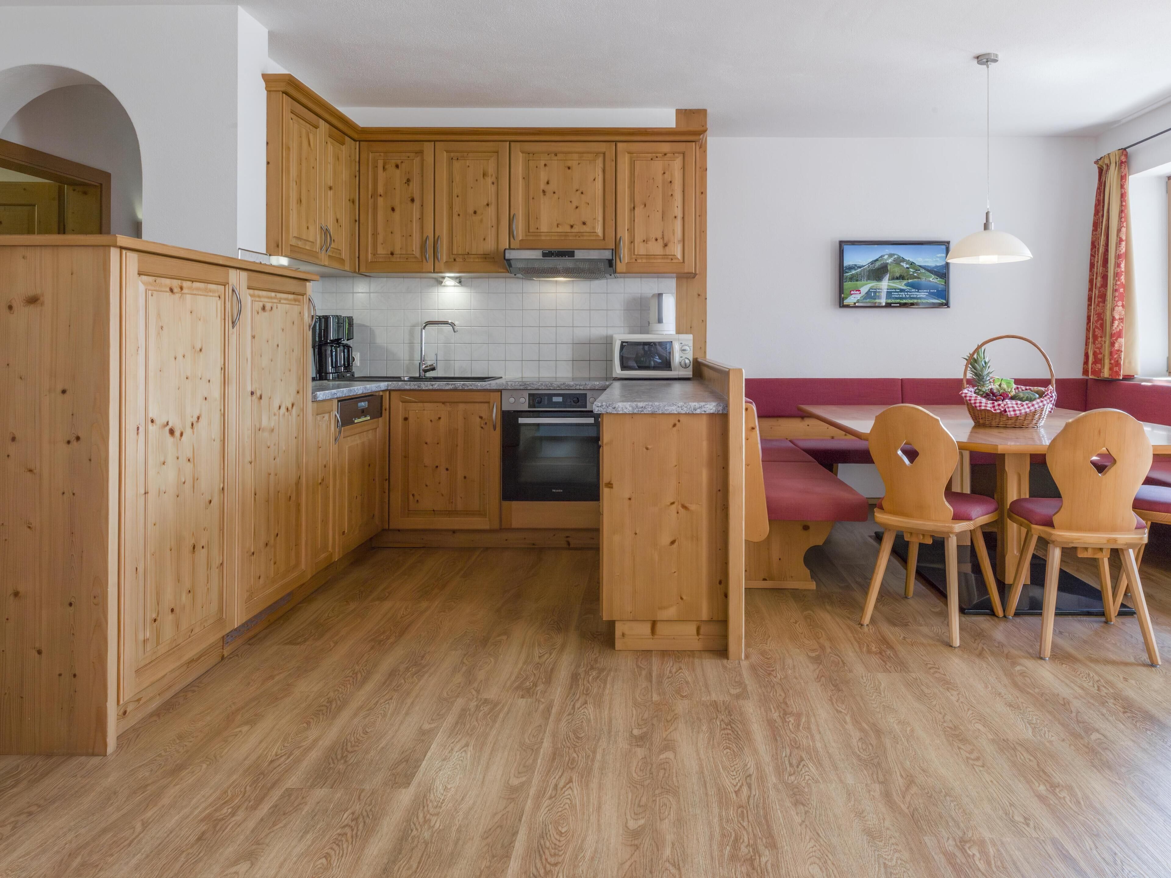 Cocina compacta con armarios de madera, un microondas y una estufa. Hay una zona de comedor con un sofá rojo y sillas de madera.