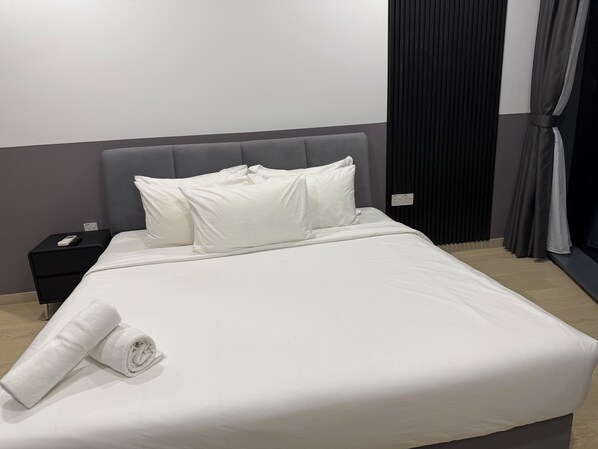 A neatly made bed with white linens and pillows, a black nightstand with a remote control, and a rolled white towel.