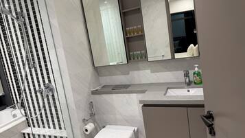 A modern bathroom with a glass shower enclosure, a toilet, a sink with toiletries, and a mirror.