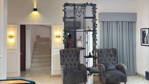 A modern living room with two grey armchairs, a small round table, a chandelier, and a staircase leading to another room. - 
3bd waterfront, Rooftops Apartment on Admiralty Lekki-ikoyi w/Pool&Gym (Lekki)