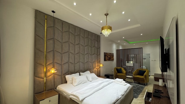 A modern bedroom with a large bed, bedside tables, a chandelier, a TV, and a seating area with chairs. - 
3bd waterfront, Rooftops Apartment on Admiralty Lekki-ikoyi w/Pool&Gym (Lekki)