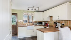 A compact kitchen with white cabinets, a wooden countertop, and a window with a patterned curtain. - Tom Callows Gorgeous Cottage Oxfordshire (Banbury)