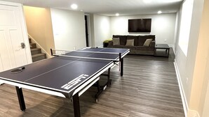 A room with two ping pong tables, a sofa, and a TV mounted on the wall.