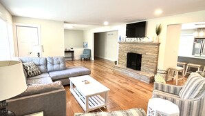 A living room with a stone fireplace, a grey sofa, a white coffee table, and a striped armchair.