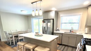 A modern kitchen with a central island, bar stools, a refrigerator, a stove, and a window providing natural light.