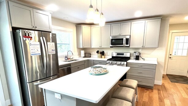 A modern kitchen with a central island, stainless steel appliances, and light wood flooring.