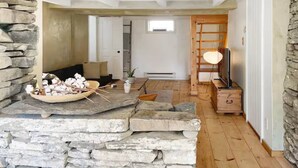 A rustic interior with stone walls, a wooden floor, a sofa, a television, and a small table with a bowl of cotton balls.