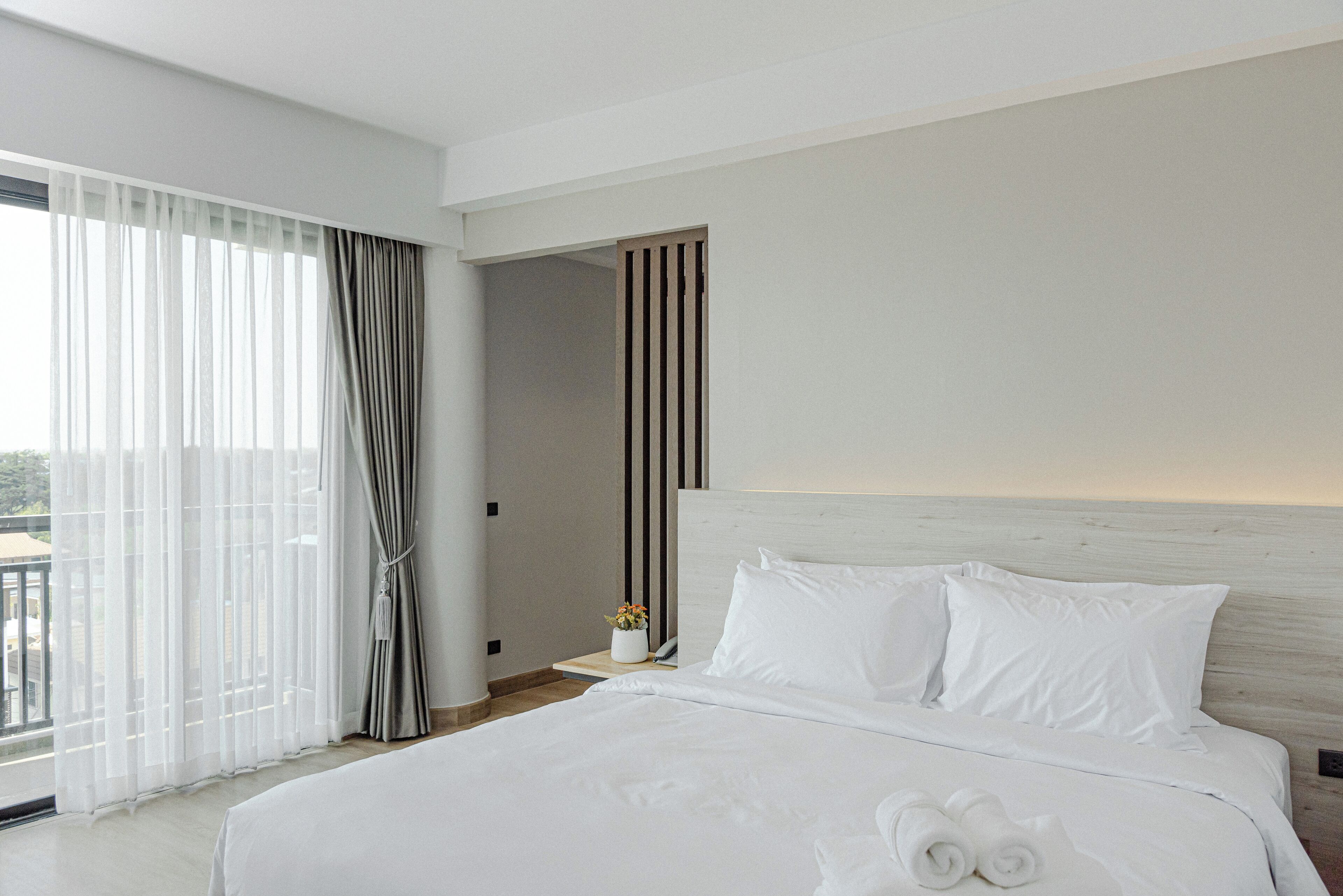Una habitación de hotel moderna con una cama grande, vistas al exterior a través de cortinas traslúcidas y un cabecero de madera.