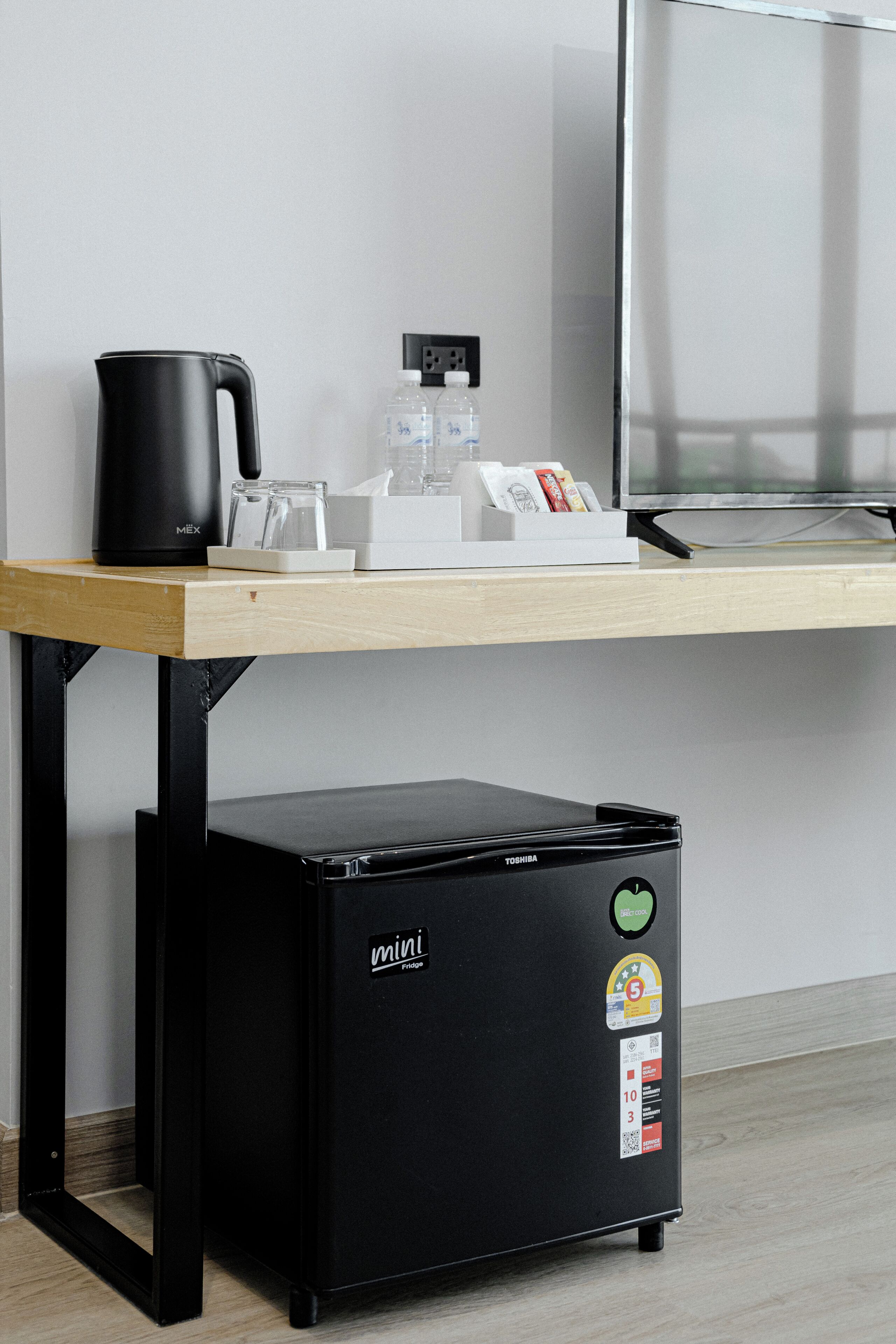 Una kitchenette con cafetera, refrigerador miniatura y microondas sobre una mesa de madera.