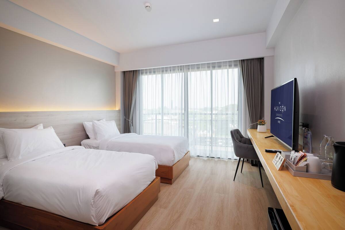 Een hotelkamer met twee bedden, een bureau, een televisie en een groot raam met gordijnen.